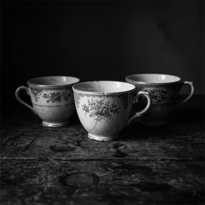 Tres tazas de té antiguas sobre una mesa rústica de madera envueltas en sombras profundas con estilo dramático.