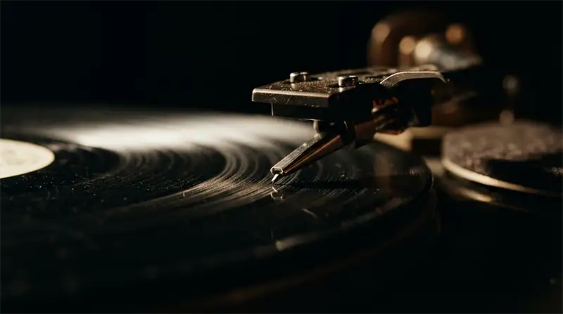 Aguja de tocadiscos descendiendo sobre el surco de un vinilo en penumbra.