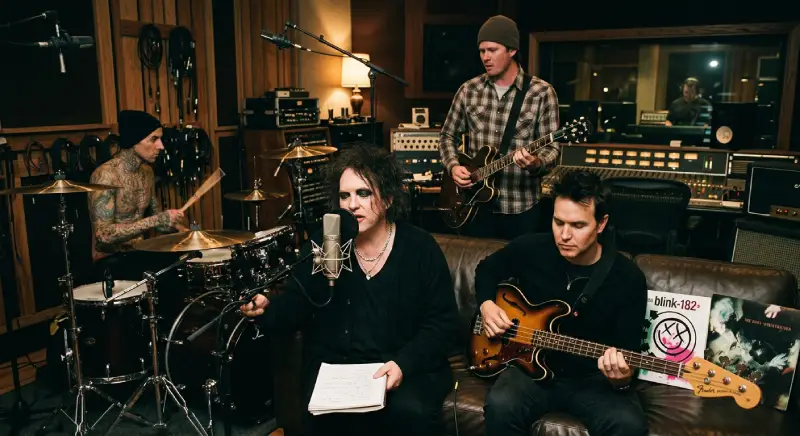 Una fotografía de Travis Barker, Robert Smith de The Cure, Tom DeLonge y Mark Hoppus, en un estudio de grabación con poca luz. Travis Barker está sin camisa y tatuado, y toca una batería. Robert Smith tiene cabello negro desordenado y delineador de ojos, y canta en un micrófono. Tom DeLonge lleva un gorro y toca una guitarra eléctrica. Mark Hoppus tiene cabello oscuro y pinchos, y toca un bajo eléctrico. En un sofá detrás de Robert Smith y Mark Hoppus, hay copias del álbum "Blink-182" de 2003 y del álbum "Disintegration" de The Cure.